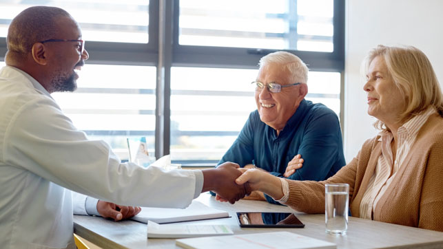 Smiling doctor shakes hands with senior couple across a table